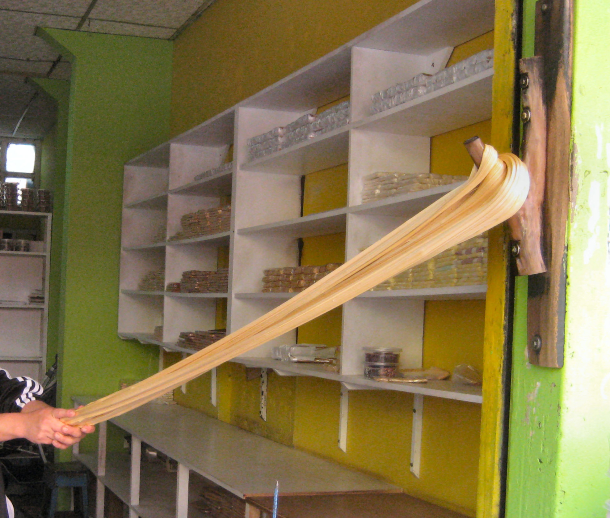Hands stretch taffy against a tree branch bolted to the wall in a traditional manner, in what appears to be a low-tech industrial kitchen.